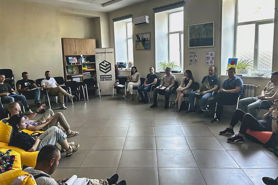 Група чоловіків і три жінки сидять у приміщенні в колі