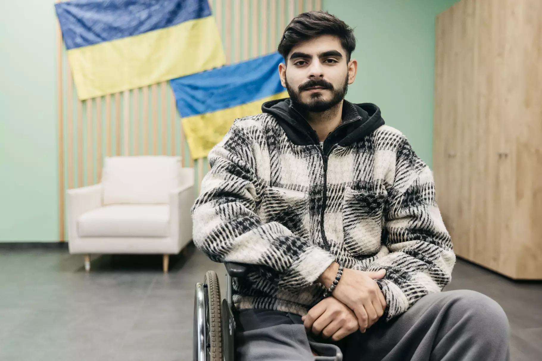 Барон сидить у кріслі колісному на фоні українських прапорів з автографами відомих людей